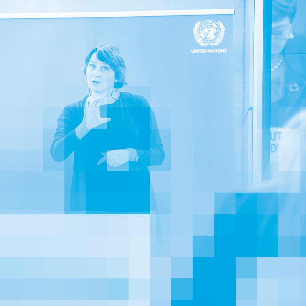 A photo, tinted in blue, of a woman standing near a podium and using sign language.