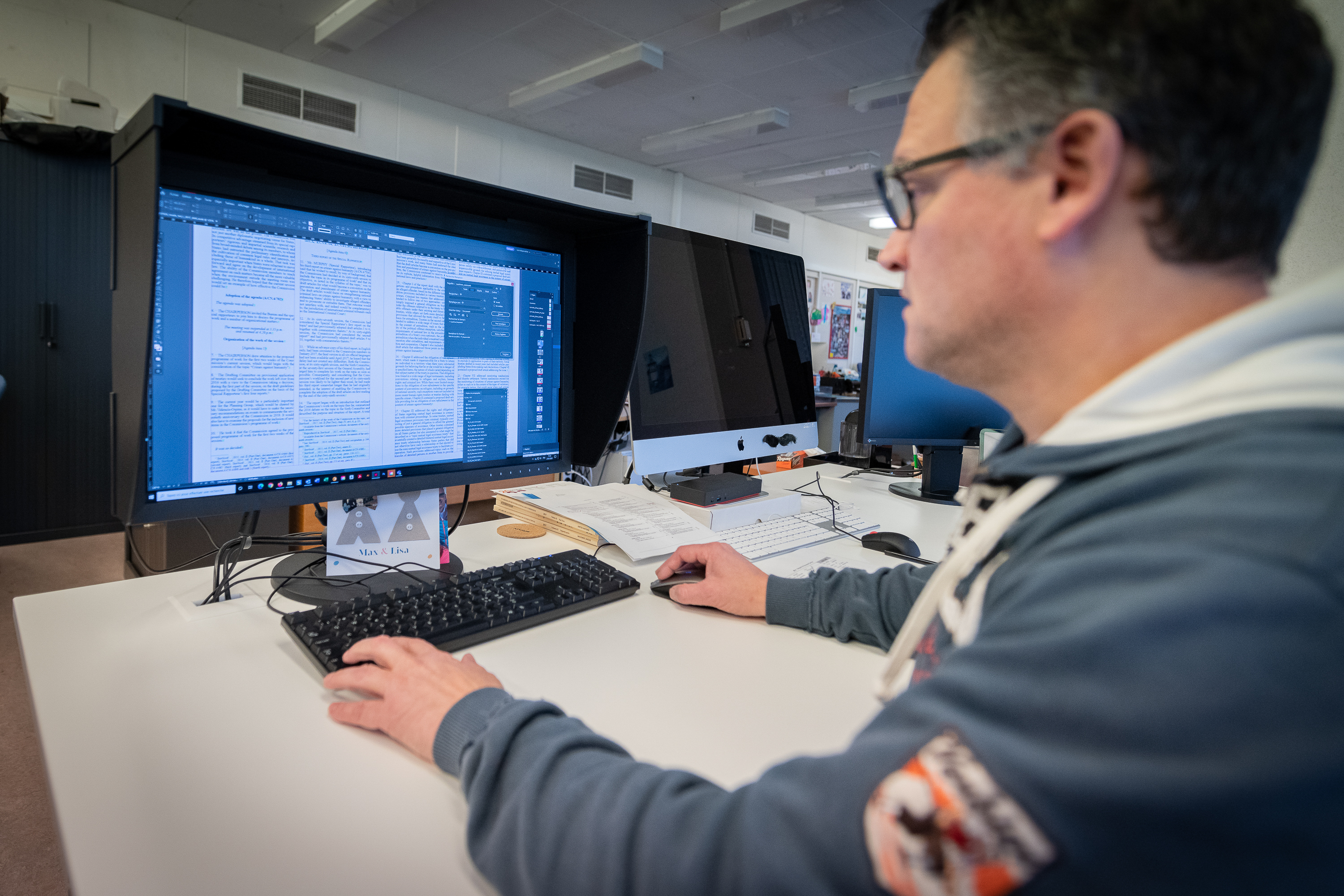Un homme est assis à un bureau et travaille sur un ordinateur. Sur l'écran de l'ordinateur, un document est ouvert.