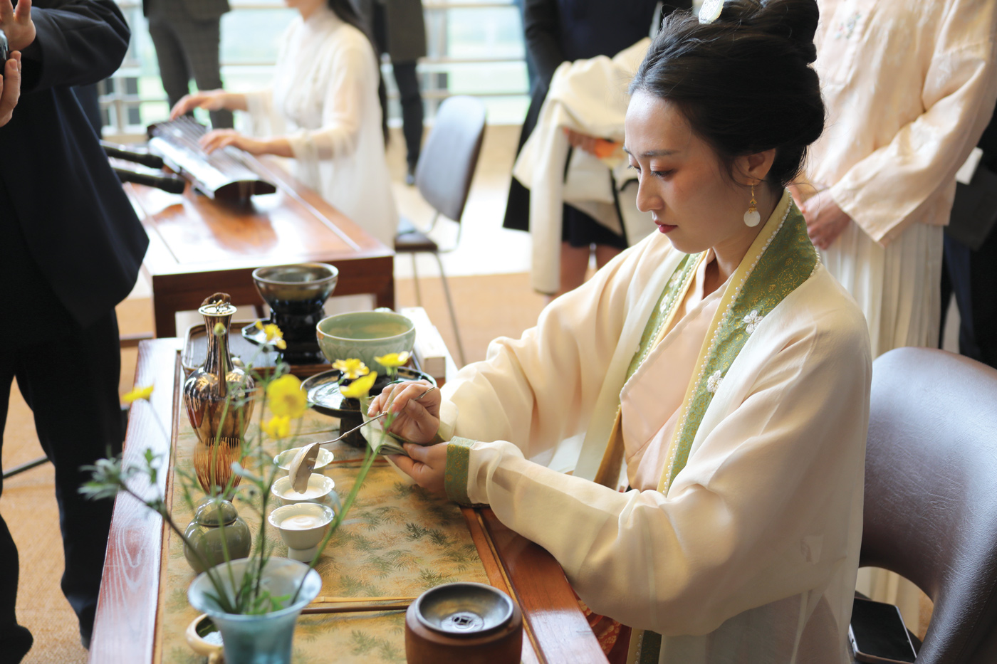 A woman is sitting at a table creating an artwork. She is wearing traditional Chinese clothes. 