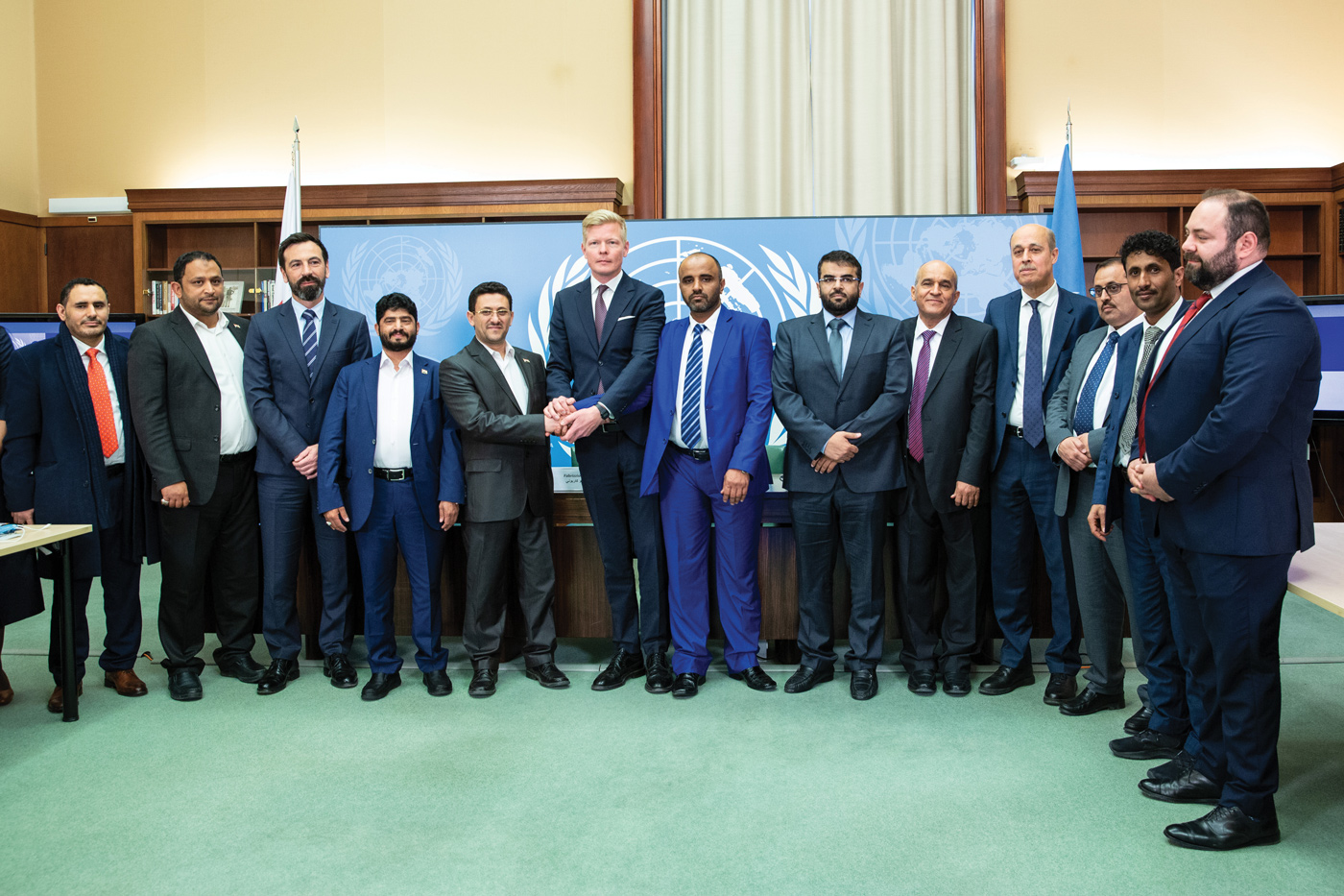 Photo showing a group of 13 men standing next to each other and posing in front of the photographer. In the middle of the group, the Special Envoy of the Secretary-General for Yemen, Hans Grundberg acknowledges a handshake between two members of the warring parties. 